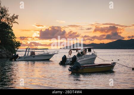 Barche da pesca riposate al tramonto luce sera vicino al porto di la Digue Island, Seychelles. Isola di Praslin all'orizzonte. Foto Stock