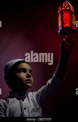 Ragazzo musulmano che tocca la tradizionale candela di lanterna araba che soffia al buio. Ragazzo mediorientale che prega. Ringraziando dio. Ramadan, Eid-al-Adha concetti Foto Stock