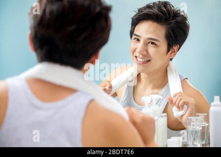 Un giovane uomo sicuro che appende un asciugamano guardare nello specchio Foto Stock