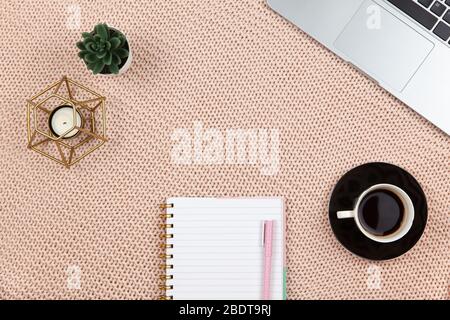 Concetto di lavoro da casa. Moderna area lavoro femminile, vista dall'alto. Laptop, cactus, candela, caffè, notebook su coperta a maglia, spazio per copia, piatto. Scrivania Foto Stock