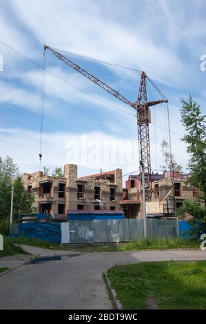 Estate in città. La costruzione di un nuovo edificio dietro una recinzione blu. Gru a torre. Non sostare sotto la freccia. Foto Stock