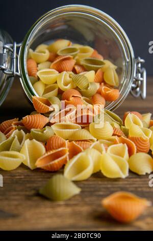 Pasta Conchiglie colorata in vaso di vetro su sfondo di legno. Vista frontale, primo piano Foto Stock