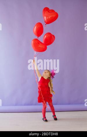 piccola bella ragazza in vacanza con palloncini rossi a forma di cuore Foto Stock