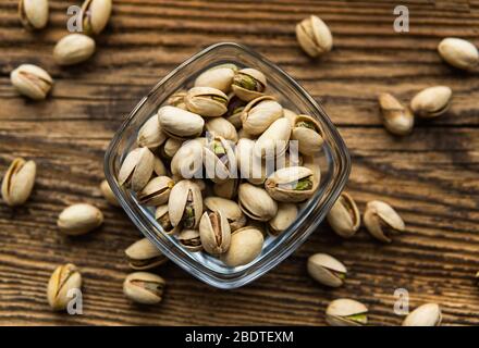 Pistacchi in un piccolo piatto con noci sparse di mandorle intorno ad un piatto su un tavolo di legno d'epoca come sfondo. Il pistacchio è un vegetariano sano Foto Stock