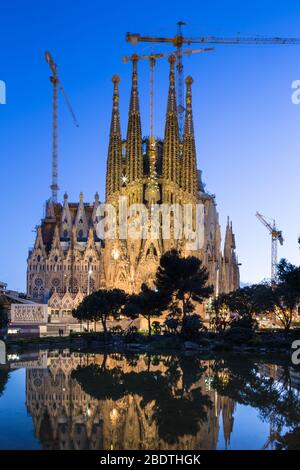 Vista del tramonto sulla facciata della Natività della basilica di la Sagra Familia riflessa nel lago della Placa de Gaudi, Barcellona, Spagna. Foto Stock