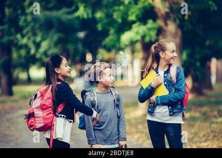 Ritorno a scuola. Chiudete tre amici felici con zaini ridenti e divertenti nel parco. Ragazzo e ragazza che tengono libri il primo giorno della scuola. Foto Stock