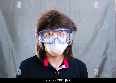 Giovane donna in maschera protettiva respiratore e occhiali protettivi blu durante l'isolamento e la quarantena. Non le piace. Rimani a casa Foto Stock