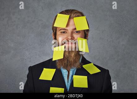 Occupato. Felice sorridente sopraffatto uomo d'affari pieno di adesivi, note, piani isolati grigio sfondo grunge Foto Stock