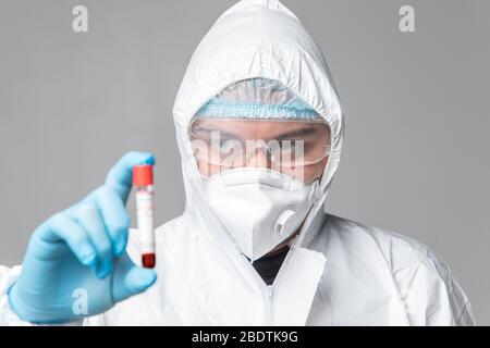 Uomo che indossa HAZMAT Abbigliamento protettivo azienda provetta riempita di sangue isolato su uno sfondo bianco. Foto Stock