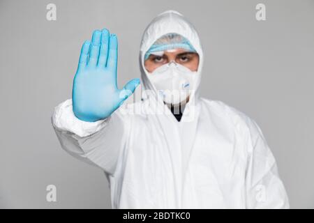 Ritratto di paramedico da un vestito protettivo del paziente della corona che dà un gesto DI ARRESTO usando le sue mani isolate su sfondo grigio. Foto Stock