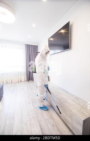 La disinfezione in tuta protettiva conduce la disinfezione in casa per prevenire il coronavirus. Auto sanitaria. Foto Stock