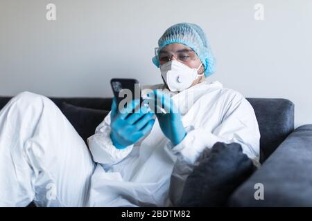 Giovane uomo in abiti a rischio biologico con il telefono e rimanendo in isolamento Foto Stock