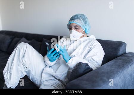 Giovane uomo in abiti a rischio biologico con il telefono e rimanendo in isolamento Foto Stock