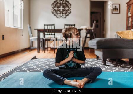 Ragazzo in età scolare che fa yoga in soggiorno durante l'isolamento Foto Stock