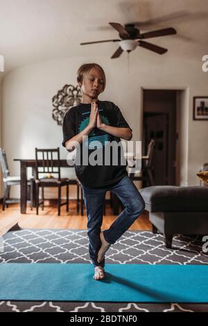 Ragazzo in età scolare che fa yoga in soggiorno durante l'isolamento Foto Stock