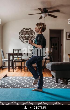 Ragazzo in età scolare che fa yoga in soggiorno durante l'isolamento Foto Stock