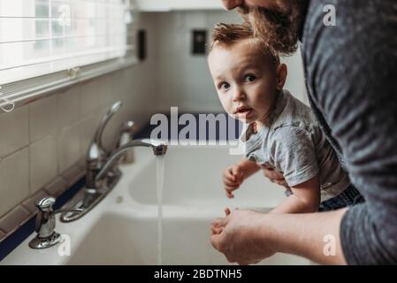 Vista laterale del ragazzo che ha le mani lavate nel lavandino da papà Foto Stock