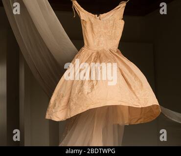 Antico abito da ballo in seta satinata appeso in aria soffiato a vento con tenda drappeggiato dietro Foto Stock