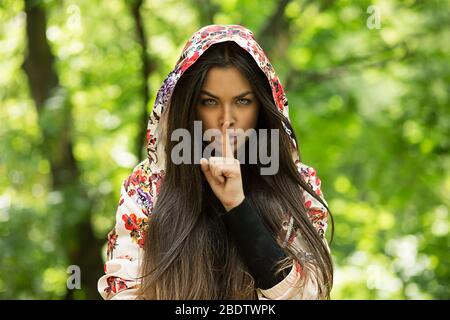 Donna con occhi spalancati che chiede silenzio o segretezza con il dito sulle labbra hush mano gesto sfondo verde parete. Bella ragazza che mette le dita sulle labbra, shhh s Foto Stock