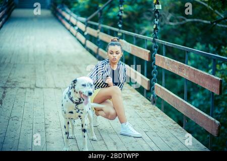 Donna ragazza con il suo cane dalmata sul ponte cercando di impedirgli di correre Foto Stock