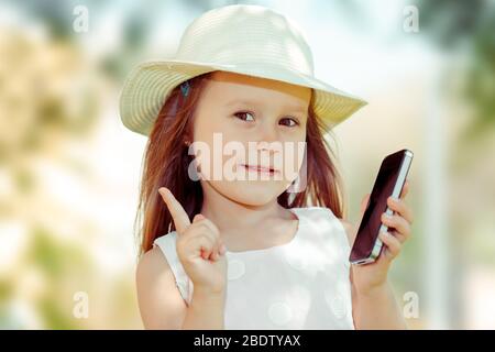 Bambino con smartphone. Ritratto closeup di bella ragazza capretto che tiene il telefono delle cellule che mostra no, non, attenzione con il gesto della mano del dito. Bloccaggio pericoloso Foto Stock