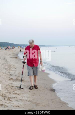 Senior maschio cammina con un rilevatore di metalli elettronico, come essere gode il suo hobby come spiaggia e cacciatore di tesori Foto Stock