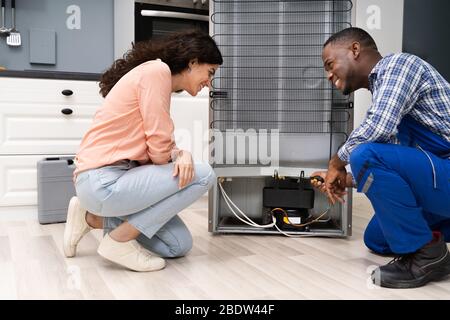 Giovani Repairman riparazione frigorifero nella parte anteriore della bella donna Foto Stock