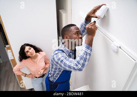 Donna felice Guardando elettricista Installazione di sicurezza sistema rivelatore di movimento sulla parete Foto Stock