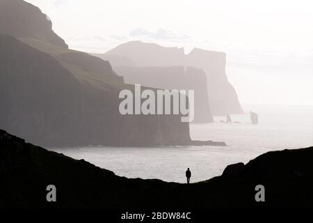 Silhouette uomo sullo sfondo del famoso Risin og Kellingin rocce e dirupi di Eysturoy e isole Streymoy visto da Kalsoy isola. Isole Faerøer, Danimarca. Fotografia di paesaggi Foto Stock