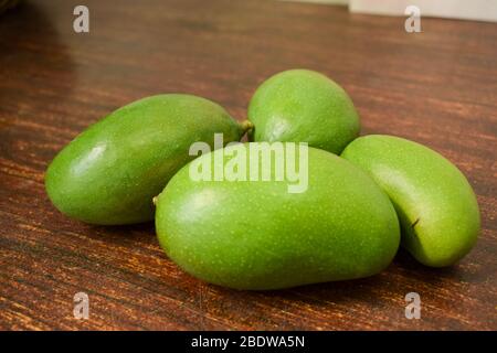 Organica giovane Mango Verde Branch Macro isolato su tavola di legno frutta acour. Foto Stock