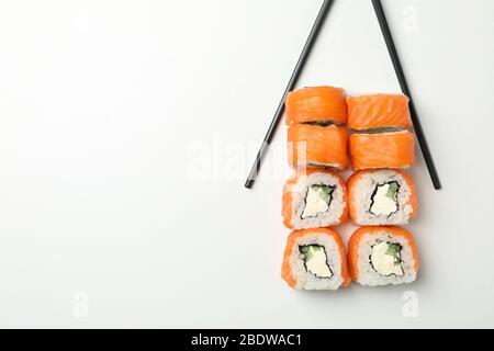 Chopsticks e sushi rotola su sfondo bianco, spazio per il testo Foto Stock