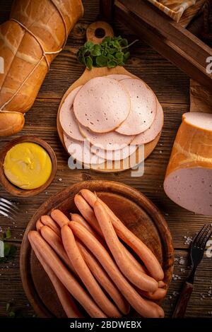 Salsicce e salumi bolliti freschi serviti con senape su tagliere in legno Foto Stock