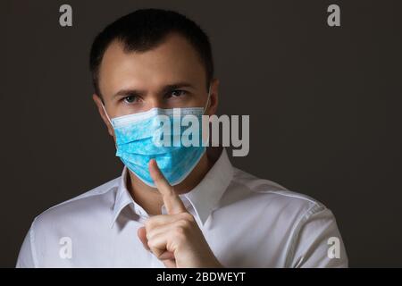 L'uomo mascherato mostra un segno di silenzio. Il concetto di coronavirus è una vera minaccia o un'isteria di massa Foto Stock