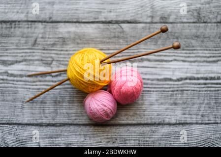 Piatto di tre palle di lana colorate, aghi di maglia che posano sullo sfondo di legno. Foto Stock