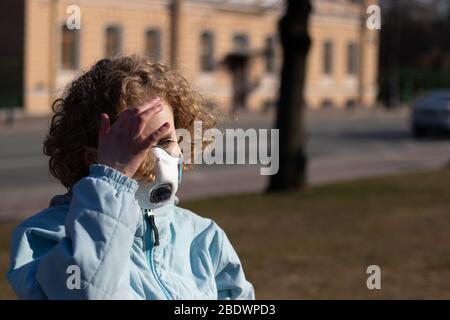 Ragazza raddrizza i capelli ricci con la mano sulla strada. Donna che indossa una maschera protettiva medica. Spazio di copia Foto Stock