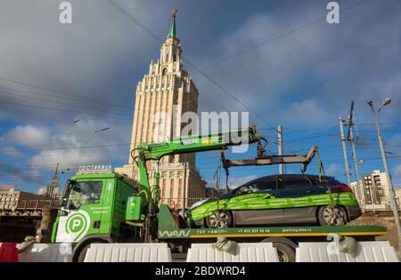 1 aprile 2019 Mosca, Russia. Un camion porta un'auto a un parcheggio sullo sfondo dell'edificio dell'hotel Leningradskaya sulla piazza di Foto Stock