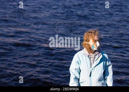 Ragazza in maschera protettiva viso guarda via su uno sfondo d'acqua. Spazio di copia per problemi di salute e concetto di virus Foto Stock