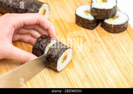 Sushi roll giapponese makis cibo tagliato da coltello tagliente su bordo di bambù Foto Stock