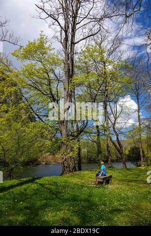 Solitaria femmina seduto su panchina di pietra del fiume Ariege, Ornolac Ussat les Bains, Ariege, Pirenei francesi, Francia Foto Stock