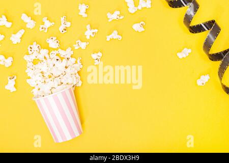 Secchio popcorn e striscia di pellicola su sfondo giallo. Film o sfondo TV. Vista superiore spazio di copia Foto Stock