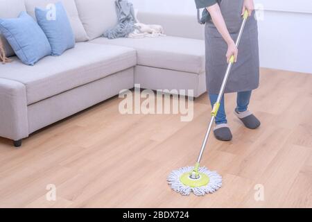 Pavimenti per mop. Giovane donna lavaggio in legno piano terra a casa con un mop, pulizia attrezzature, concetto di antibatterico, prevenzione virus, primo piano. Foto Stock