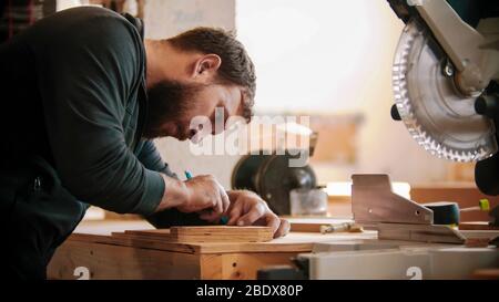 Falegnameria lavorazione - uomo barbuto che fa segni sul compensato. Scatto intermedio Foto Stock