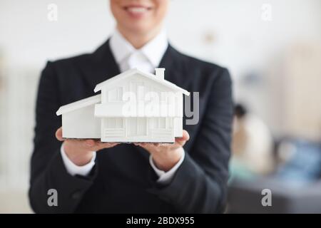 Primo piano di donna d'affari in abito nero che tiene modello della casa nelle sue mani Foto Stock