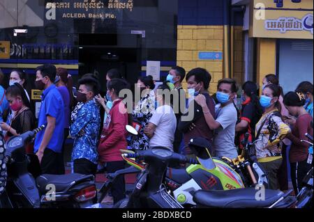 Nessun divaricamento sociale, caos come lavoratori cambogiani di fabbrica di indumenti, indossando maschere di protezione viso / coperture, allinearsi in su ad una banca il 1 ° giorno Phnom Penh chiude tutte le strade in e fuori della città prima cambogiano Capodanno durante la pandemia coronavirus. Steung Meanchey, Phnom Penh, Cambogia. 10 aprile 2020. © Kraig Lieb Foto Stock