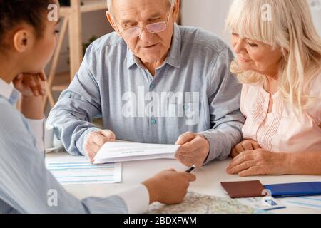 Agente di viaggio in ufficio seduto con i clienti senior uomo lettura contratto concentrato primo piano Foto Stock