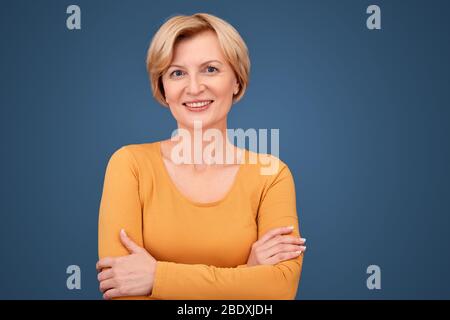 Stile libero. Donna matura in piedi isolata su mani blu incrociate sorridendo fiducioso Foto Stock