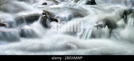 Ruscelli d'acqua splendidamente a cascata lungo un piccolo fiume selvaggio, formato panoramico e lunga esposizione per il flusso astratto Foto Stock