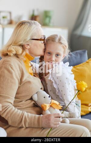 Nonna seduta sul divano e baciare la sua nipote che dà un regalo per lei a casa Foto Stock