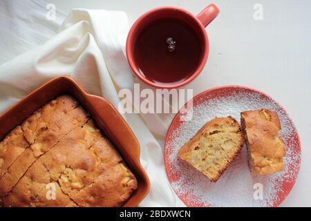 Tradizionale budino di mela di Charlotte appena sfornato in teglia e su un piatto con zucchero in polvere. Torta leggera e una tazza di tè per la colazione. Foto Stock
