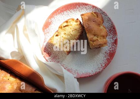 Tradizionale budino di mela di Charlotte appena sfornato in teglia e su un piatto con zucchero in polvere. Torta leggera e una tazza di tè per la colazione. Foto Stock